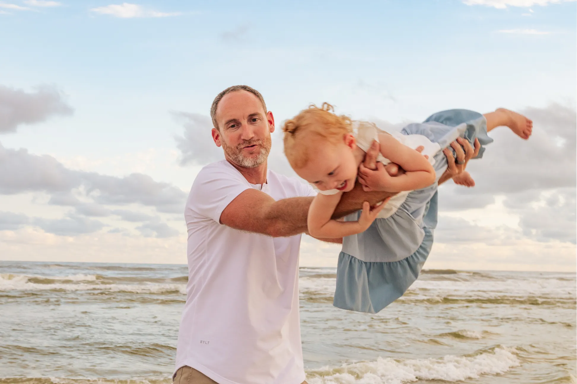 Father flying his daughter around like a airplane during a Gulf Shores family beach photoshoot..