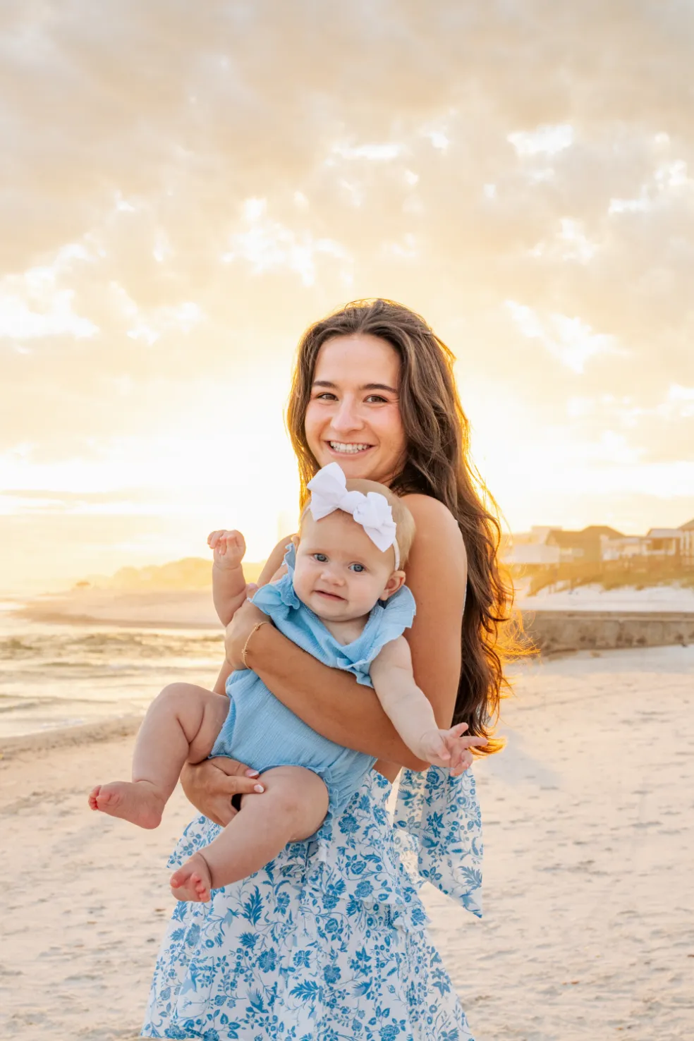 Young woman holding her baby sister while standing for a photo during a Gulf Shores family beach photoshoot.