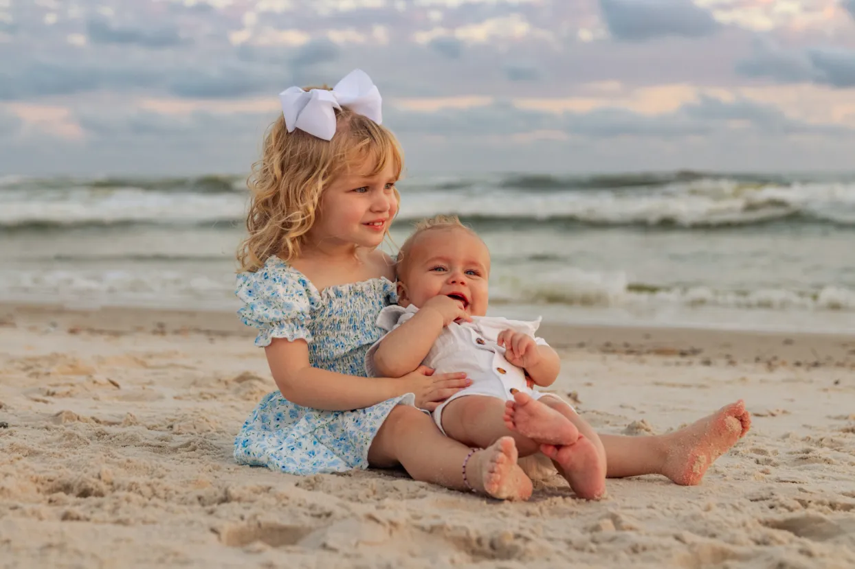 A young girl holding her baby brother in her arms during a Gulf Shores family beach photoshoot..