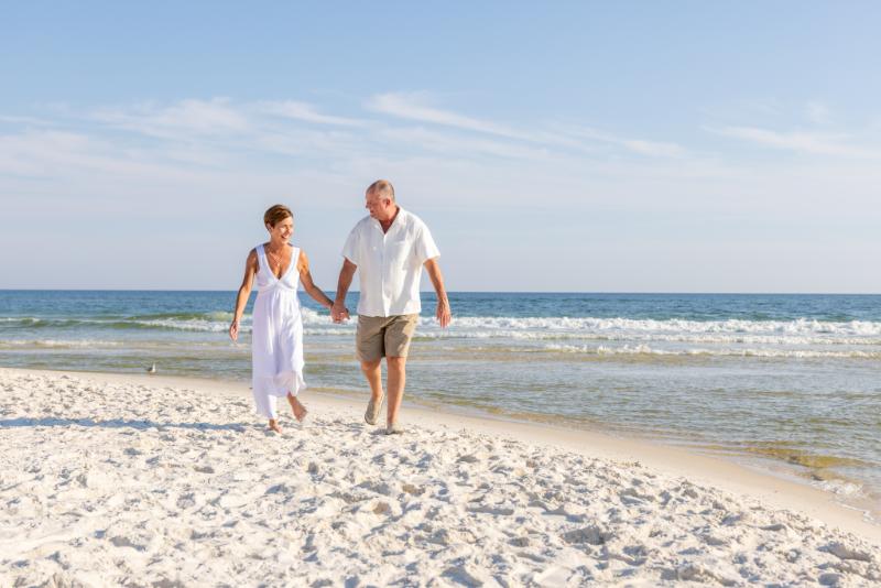 Anniversary photoshoot in Gulf Shores, Alabama. A married couple walking the beach holding hands wearing all white. Gulf Shores anniversary photographer